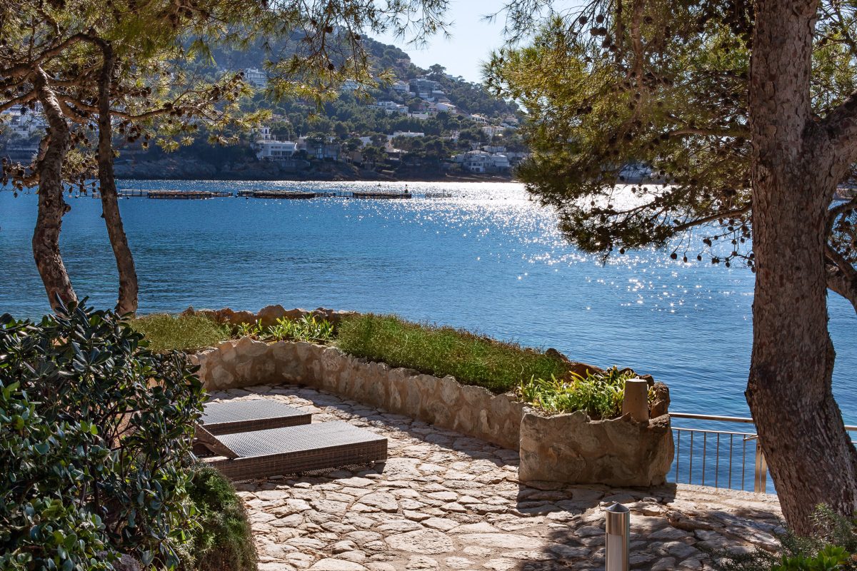 27 An image of a stunning frontline home in Port Andratx, featuring direct access to the water and a private boathouse. The home is designed with sleek, modern architecture, offering expansive windows that provide breathtaking views of the harbor and Mediterranean Sea. The boathouse is ideally located on the property, allowing for easy docking and access to water activities. The beautifully landscaped outdoor space includes a private terrace, pool, and lounge areas, creating an exclusive, luxurious waterfront retreat.